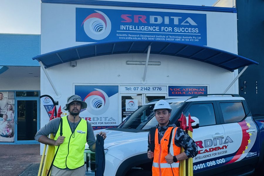 Two SRDITA students with surveying equipment beside an SRDITA vehicle outside the campus