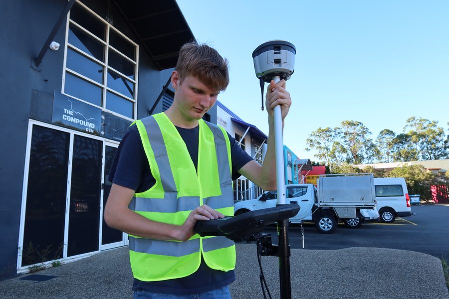 A student using a GNSS rover and field controller beside the SRDITA building