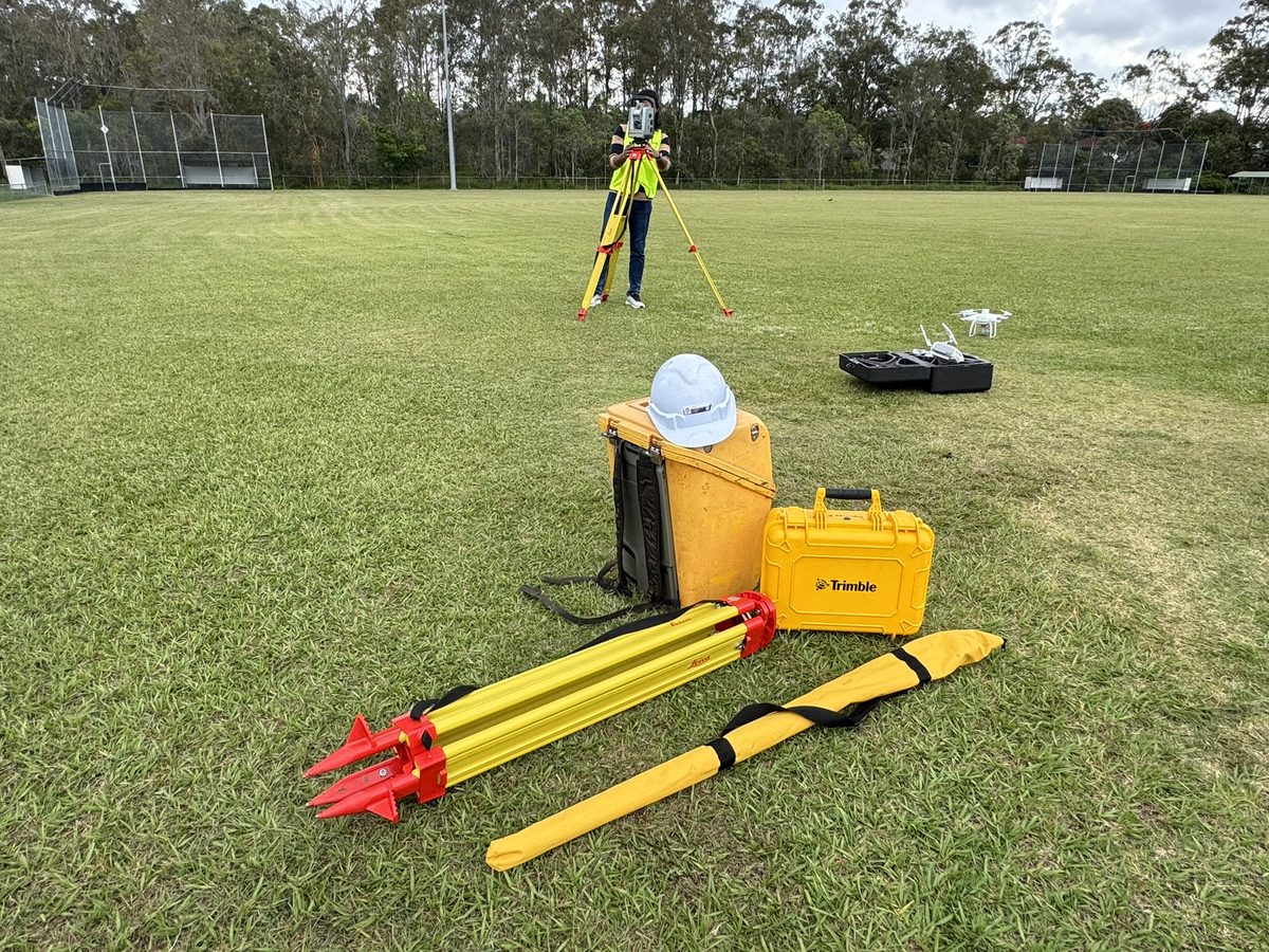 Survey equipment laid out on a field: tripod, ranging poles, GNSS and total station cases