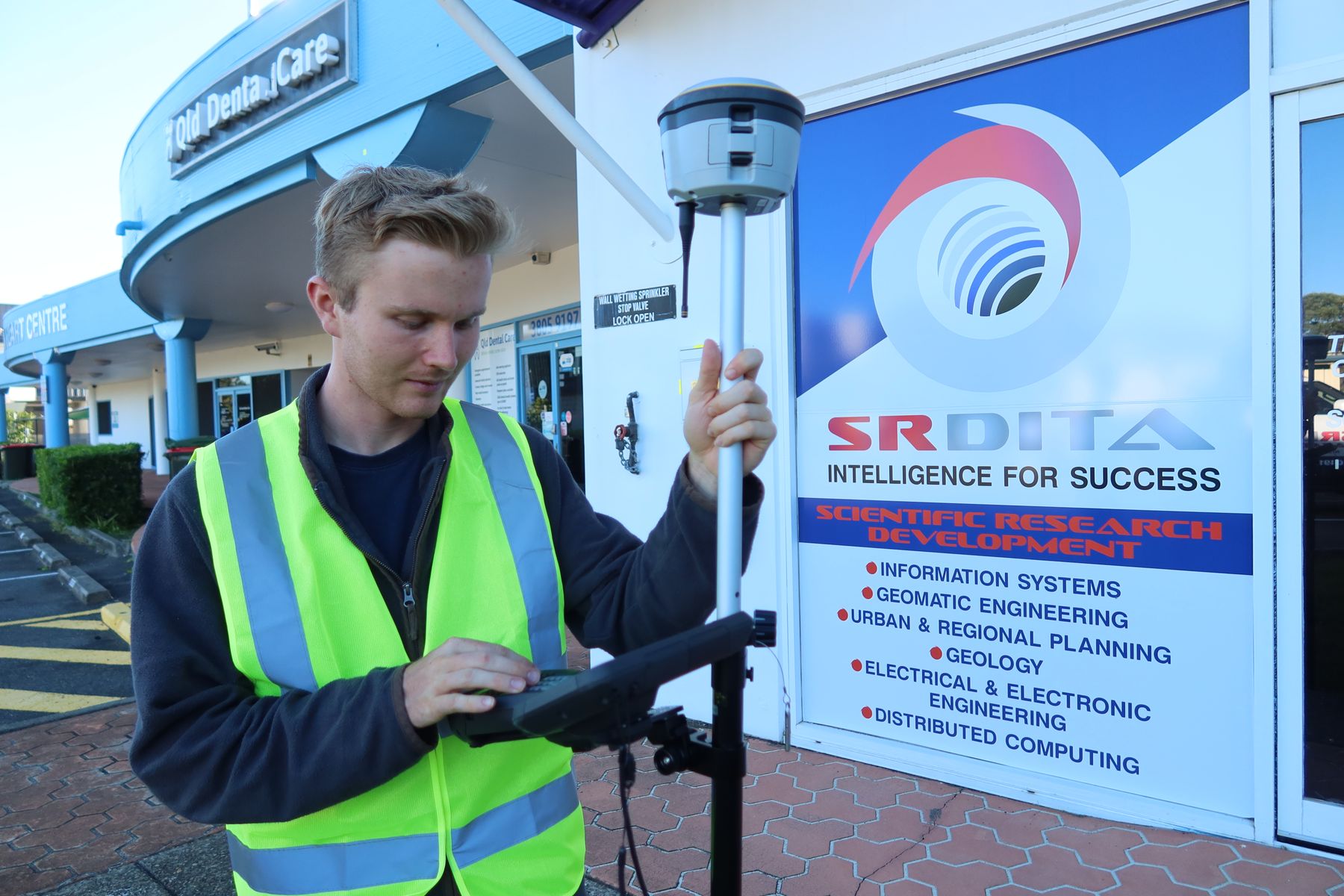 An SRDITA student using a GNSS rover and field controller outside the SRDITA building